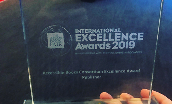 Foto do troféu do prêmio que a Maluhy & Co. ganhou, trofeu em vidro com o logo do  International Excellence Awards 2019
